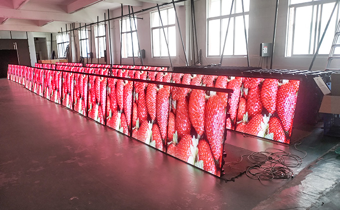 Rows of perimeter LED displays (led screen) in a factory, showing vivid strawberry visuals. Highlights the led display\'s brightness and clarity for outdoor or event perimeter use.